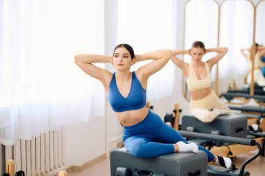 İki kadın iyi aydınlatılmış bir stüdyoda güç ve esneklik göstererek pilates egzersizleri yapıyor..
