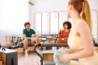 Katılımcılar iyi aydınlatılmış bir stüdyo ortamında dinamik bir pilates oturumunda odaklanıyorlar.
