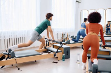 Katılımcılar güneşli bir stüdyoda pilates reformcularını kullanarak vücutlarını esnetip güçlendiriyorlar..