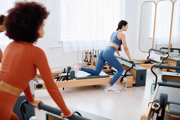 Участники тренируются на пилатесе в хорошо освещенной студии, погружаясь в целенаправленные тренировки.