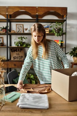 Sıcak bir odada, genç bir kadın bağışlanmak için kıyafetleri düşünceli bir şekilde sınıflandırıyor, sürdürülebilirliği destekliyor..