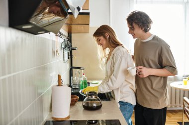 Genç bir çift, güzel mutfaklarında kahve yaparken kahkahalarını paylaşıyor..