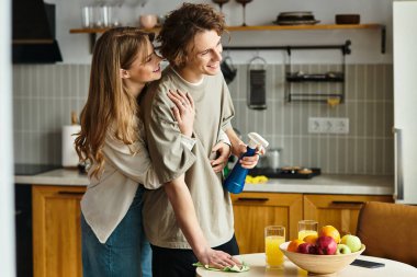 Sıcak bir mutfakta, sevgi dolu bir çift temizlik yaparken gülümser ve neşeli anlar paylaşır..