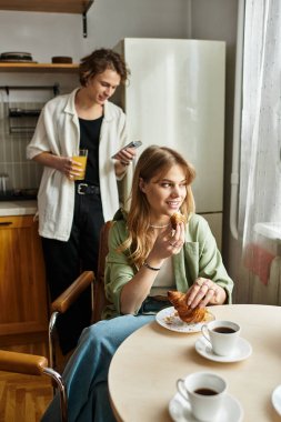 A young couple shares a joyful breakfast moment at home, savoring delicious croissants and coffee. clipart