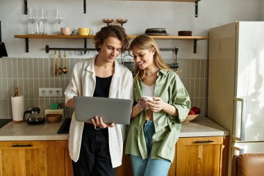 Genç çift evde gülümsüyor, dizüstü bilgisayarla çalışıyor ve birlikte kahvenin tadını çıkarıyor..