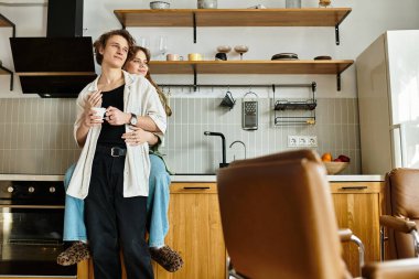 Sevgi dolu çift, rahat mutfaklarında sıcak bir anı paylaşır, içkilerini yudumlarken kucaklaşırlar..