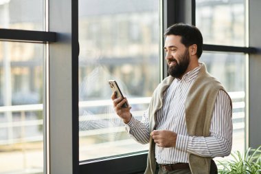 Yakışıklı yaşlı adam akıllı telefonunu kontrol ederken rahatlıyor, pencerenin yanındaki güneş ışığının tadını çıkarıyor.