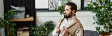 Yakışıklı yaşlı adam sıcak bir içecek tutuyor, bitkilerle dolu şık bir odayı yansıtıyor..
