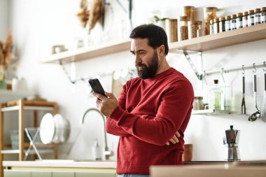 Yaşlı bir adam, büyüleyici bir dekorla güneşli bir mutfakta akıllı telefonunu karıştırarak rahatlıyor..