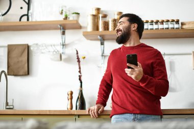 Sıcak bir gülümsemesi olan yaşlı bir adam büyüleyici bir mutfakta telefonuyla eğleniyor..