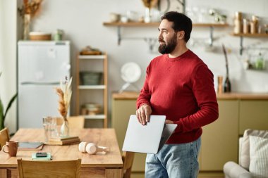 Yaşlı bir adam şık mutfağında elinde bir dizüstü bilgisayarla dikiliyor..