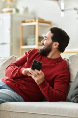 Yaşlı adam rahat bir şekilde uzanır, gülümseyerek sıcak, davetkar bir odada akıllı bir telefon tutar..