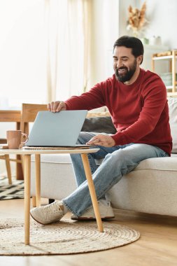 Yakışıklı son sınıf öğrencisi evde rahat rahat otururken gülümsüyor ve laptopuyla meşgul oluyor..