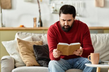Yaşlı yakışıklı bir adam rahat bir yaşam alanında otururken kitap okumaktan zevk alır..