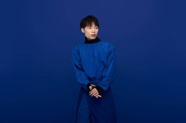 Şık bir Asyalı genç adam kendine güvenerek şık mavi bir elbise içinde poz veriyor, karizma yayıyor..