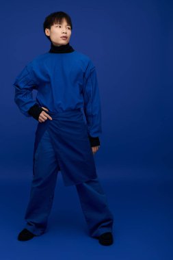 Mavi elbiseli kendine güvenen genç adam, tarzını ve yüz ifadesini göstererek cesurca poz veriyor..