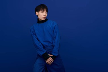 Kendine güvenen genç Asyalı adam çarpıcı mavi bir arka plana karşı şık bir görünüm sergiliyor..