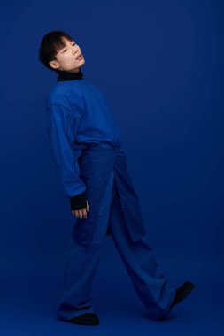 Genç, yakışıklı Asyalı bir adam şık bir mavi elbiseyle eğilir, büyüleyici ve kendine güvenlidir..