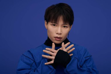 Yakışıklı Asyalı genç bir adam dikkat çekici mavi bir ortamda sanatsal bir yetenekle özgüvenle poz veriyor..