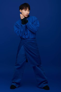 Yakışıklı Asyalı genç bir adam, kendine güvenen mavi bir elbise içinde sanatsal yeteneğini ifade ediyor..