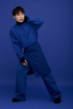 Çekici bir Asyalı genç adam canlı bir arka plana karşı şık bir mavi elbiseyle poz veriyor..