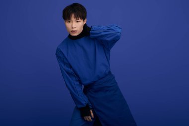 Şık bir Asyalı genç adam çarpıcı bir mavi arka plana karşı poz verirken modern moda sergiliyor..