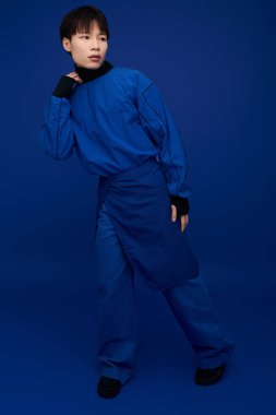 Şık mavi kıyafetli, kendine güvenen Asyalı genç bir adam canlı bir arka plana karşı..