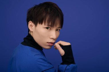 Yakışıklı genç bir Asyalı zengin bir mavi zemine karşı düşünceli bir şekilde poz verir..