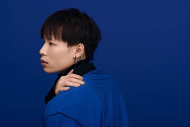 Çekici bir Asyalı genç adam parlak mavi bir arka plana karşı poz veriyor..