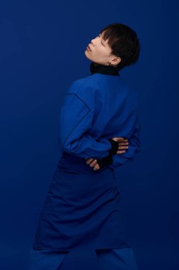 Genç yakışıklı bir Asyalı şık bir elbise içinde parlak mavi bir arka plana karşı poz veriyor..