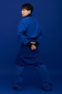 Kendine güveni tam, mavi elbiseli genç adam, elleri arkada, cazibesini sergiliyor..