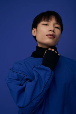 Şık bir genç adam zarif bir şekilde duruyor çarpıcı mavi bir elbiseyle, modern bir estetik sergiliyor..