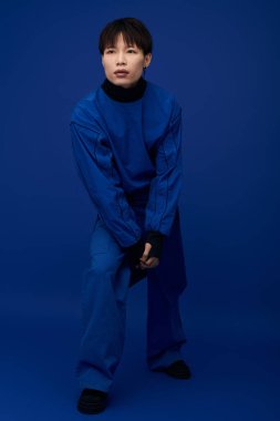 Cesur mavi kıyafetli genç bir Asyalı canlı bir arkaplana karşı güvenle poz verir..