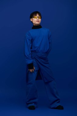 Genç yakışıklı Asyalı bir adam canlı mavi bir elbise ve güneş gözlüğü takarken kendine güvenir..