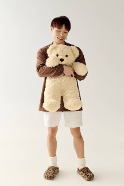 Hoş bir genç adam hafif bir boşlukta yumuşak bir oyuncak ayıyı tutarken gülümsedi..