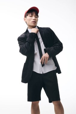 Tarz sahibi genç Asyalı adam kravatını ve ceketini stüdyoda neşeli bir ifadeyle düzeltiyor..