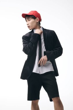 Genç, yakışıklı Asyalı bir adam kendine güvenerek şık bir ceket, şort ve şapka giyiyor..