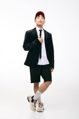 Şort üzerine şık siyah bir ceket giyen kendine güvenen genç adam stüdyoda poz veriyor..