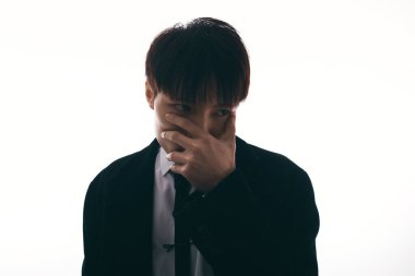 Resmi giyinmiş genç çekici bir adam hafif bir arka plana karşı derin düşünceleri yansıtır..