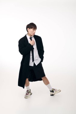 Yakışıklı bir Asyalı genç adam, uzun bir palto ve şortla modern moda elbisesi sergiliyor..