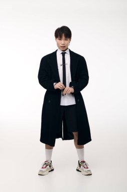 Moda kıyafetli genç yakışıklı bir adam minimalist stüdyo ortamında karizma yayıyor.