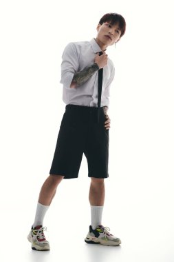 Parlak bir ortamda modern modayı gösterirken şık Asyalı genç adam kravatı ayarlıyor.