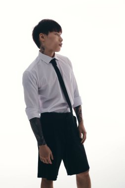 Zarif Asyalı genç adam, temiz bir arkaplana karşı şık bir ortamda güven içinde poz veriyor..