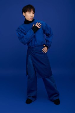 Genç ve çekici bir adam moda anlayışını sergiliyor, mavi elbiseli sanatsal bir poz yakalıyor..