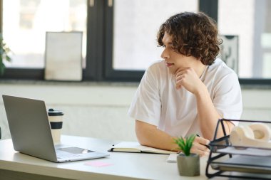 Yakışıklı genç profesyonel, şık bir ofis masasında dizüstü bilgisayarı ve not defteriyle çalışıyor.