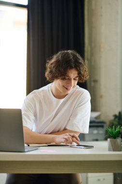 Genç ve yakışıklı bir adam şık bir ofis masasında dizüstü bilgisayarı ve bitkisi ile meşgul..