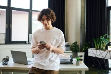 Çekici genç adam şık bir ofiste duruyor, çalışırken akıllı telefonuna odaklanıyor..