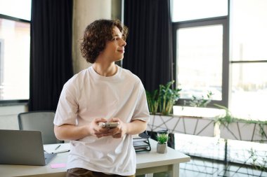 Yakışıklı genç bir adam şık bir ofiste elinde akıllı bir telefonla dikiliyor ve görevlerine odaklanıyor..