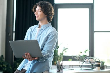 Kendine güvenen genç adam, bilgisayarını parlak bir ofiste çalışarak gününü güzelleştiriyor..