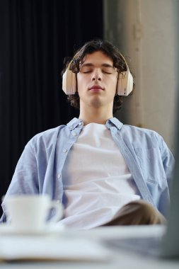 Sıradan giyinen yakışıklı adam iş yerinde kulaklık takarken rahatlıyor ve konsantre oluyor..